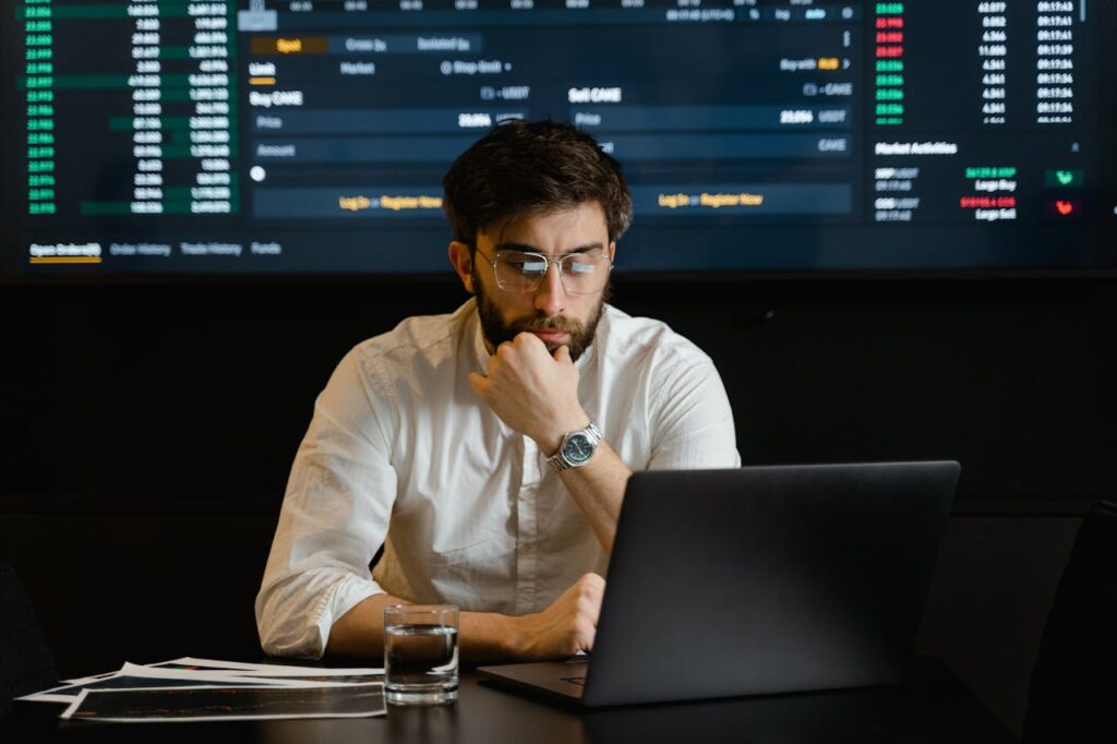 pexels-photo-7567535 A man intensely analyzing stock market data on a laptop in an office setting.